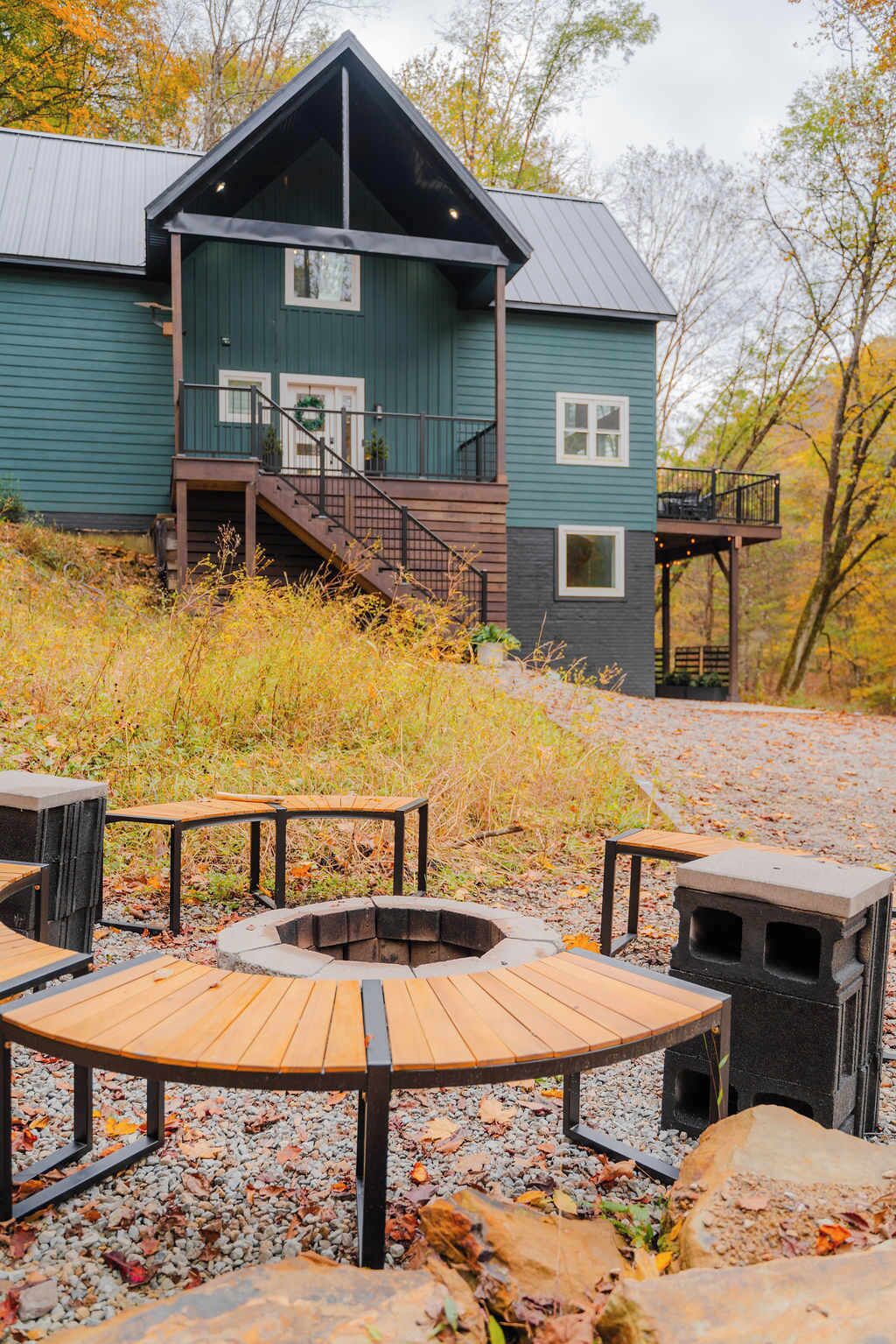 A two-story cabin with a wooden deck and a fire pit.