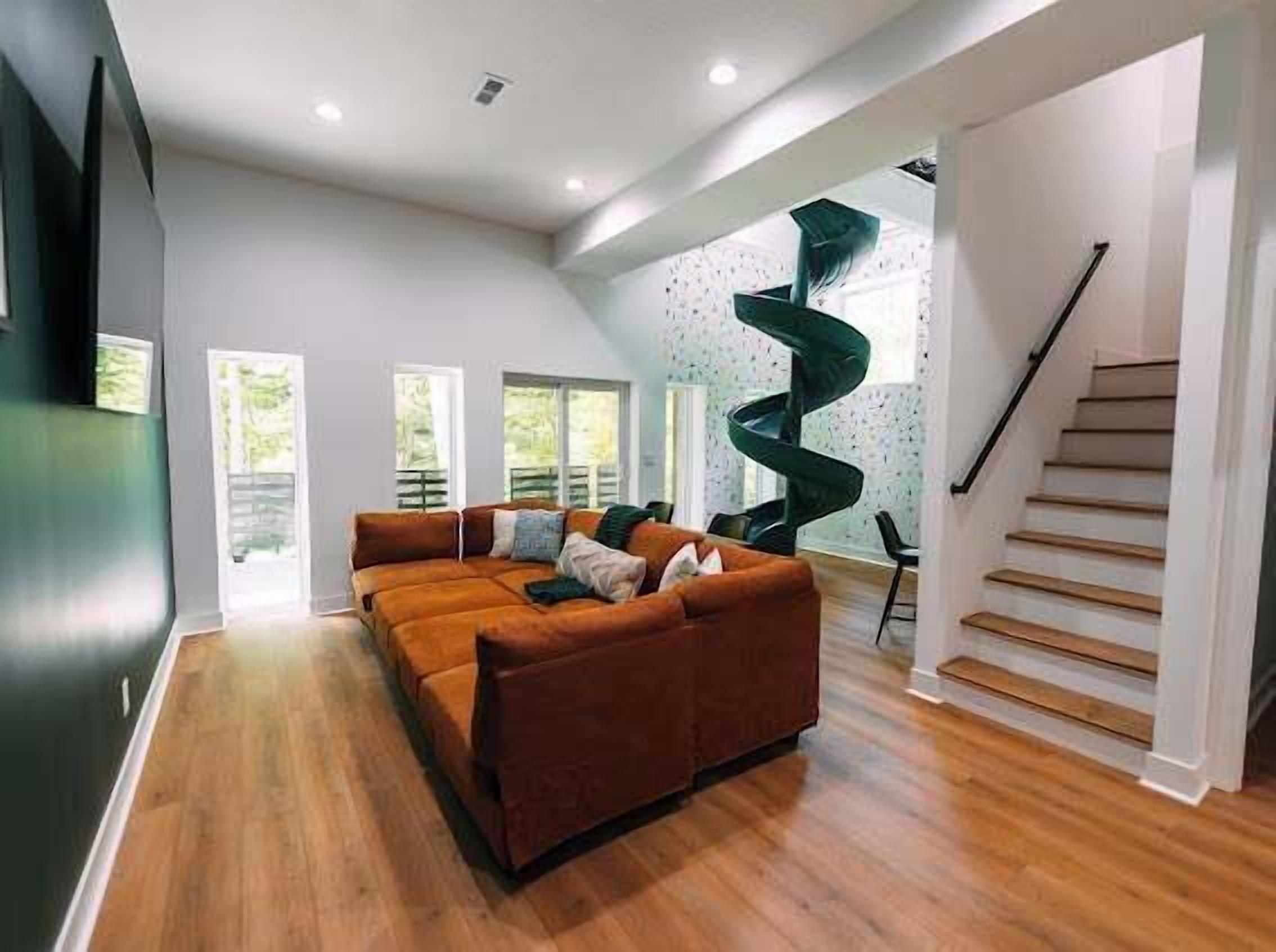 A modern living room with a brown sectional sofa, a spiral staircase, and large windows.