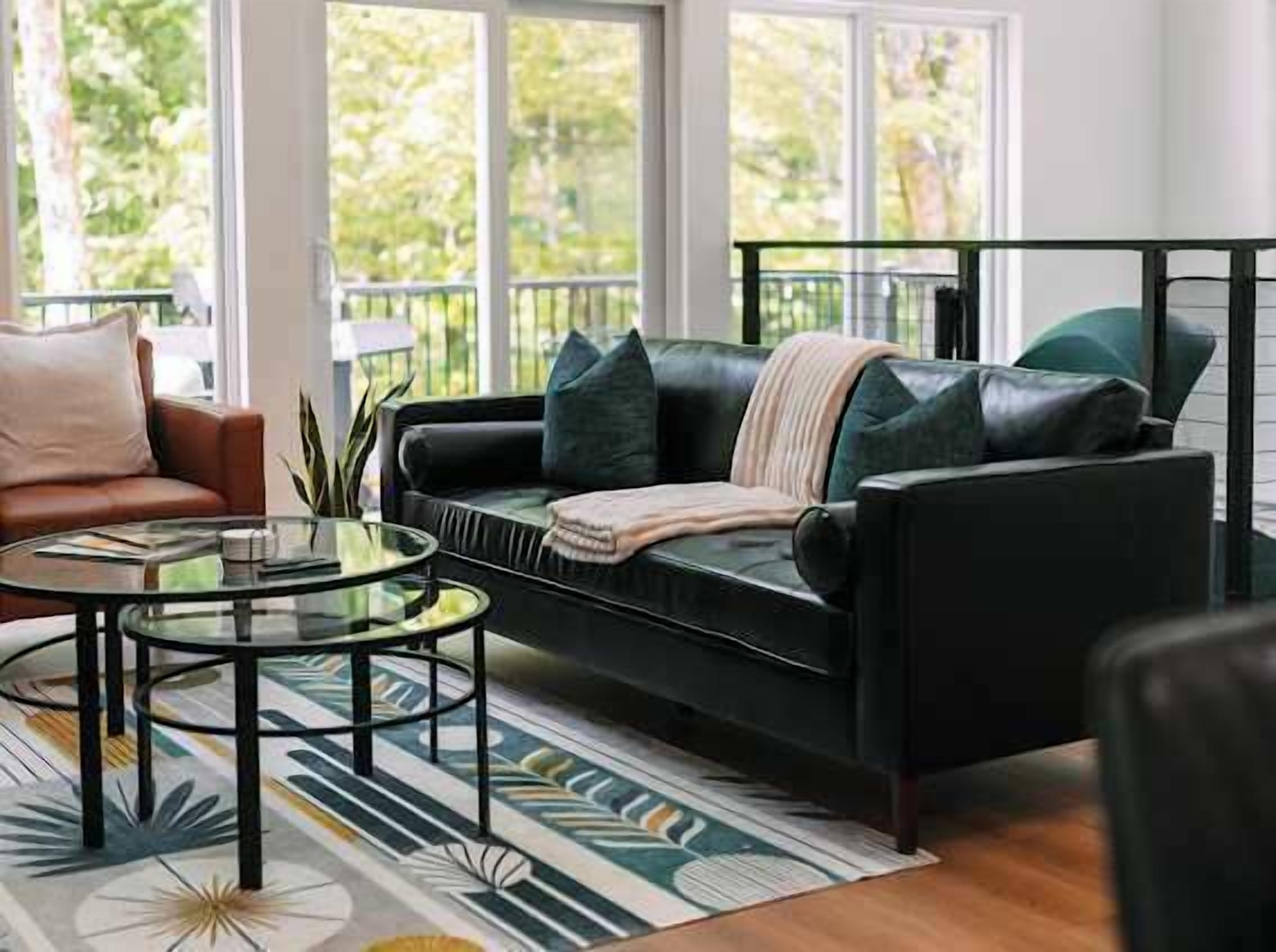 A modern living room with a black leather sofa, a glass coffee table, and a patterned rug.