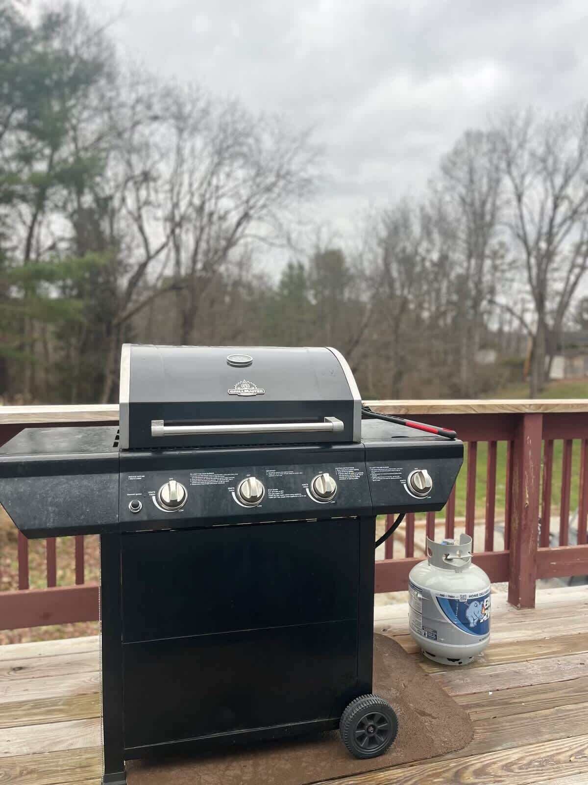 A black barbecue grill with four burners and a side burner, placed on a wooden deck with a railing in the background.