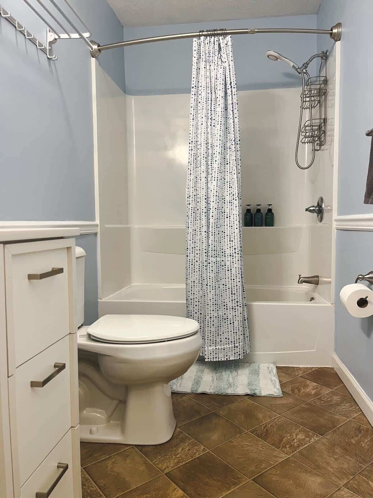 A bathroom with a toilet, a shower with a curtain, and a bathtub.