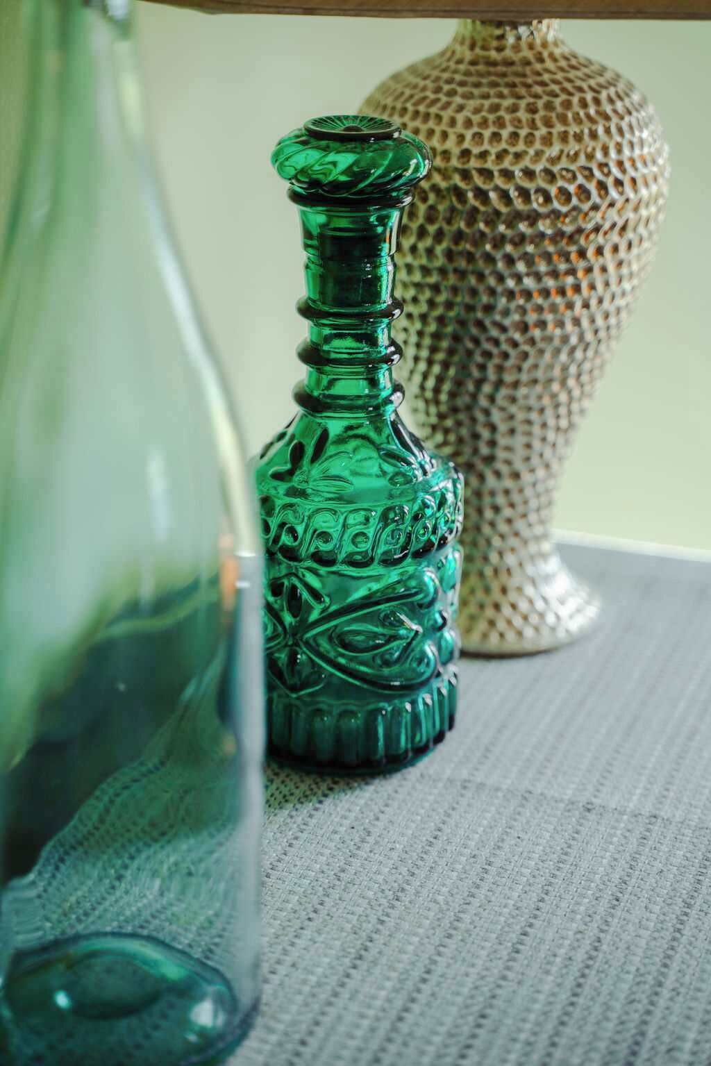 Eine grüne Glasflasche mit strukturierter Oberfläche, auf einer ebenfalls strukturierten Unterlage platziert.