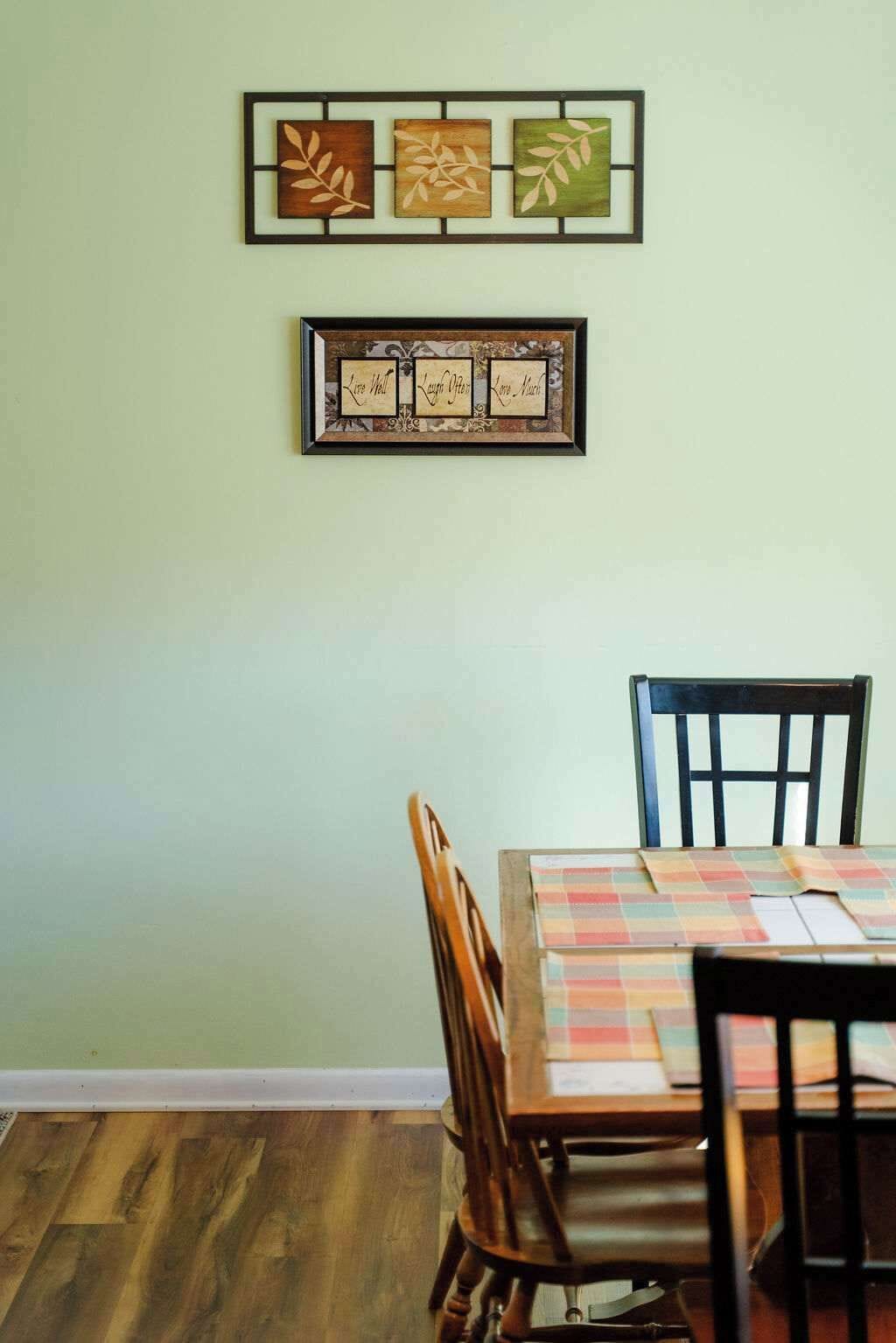 Een eetgedeelte met een tafel gedekt voor vier personen, kunstwerken erboven en een houten vloer.