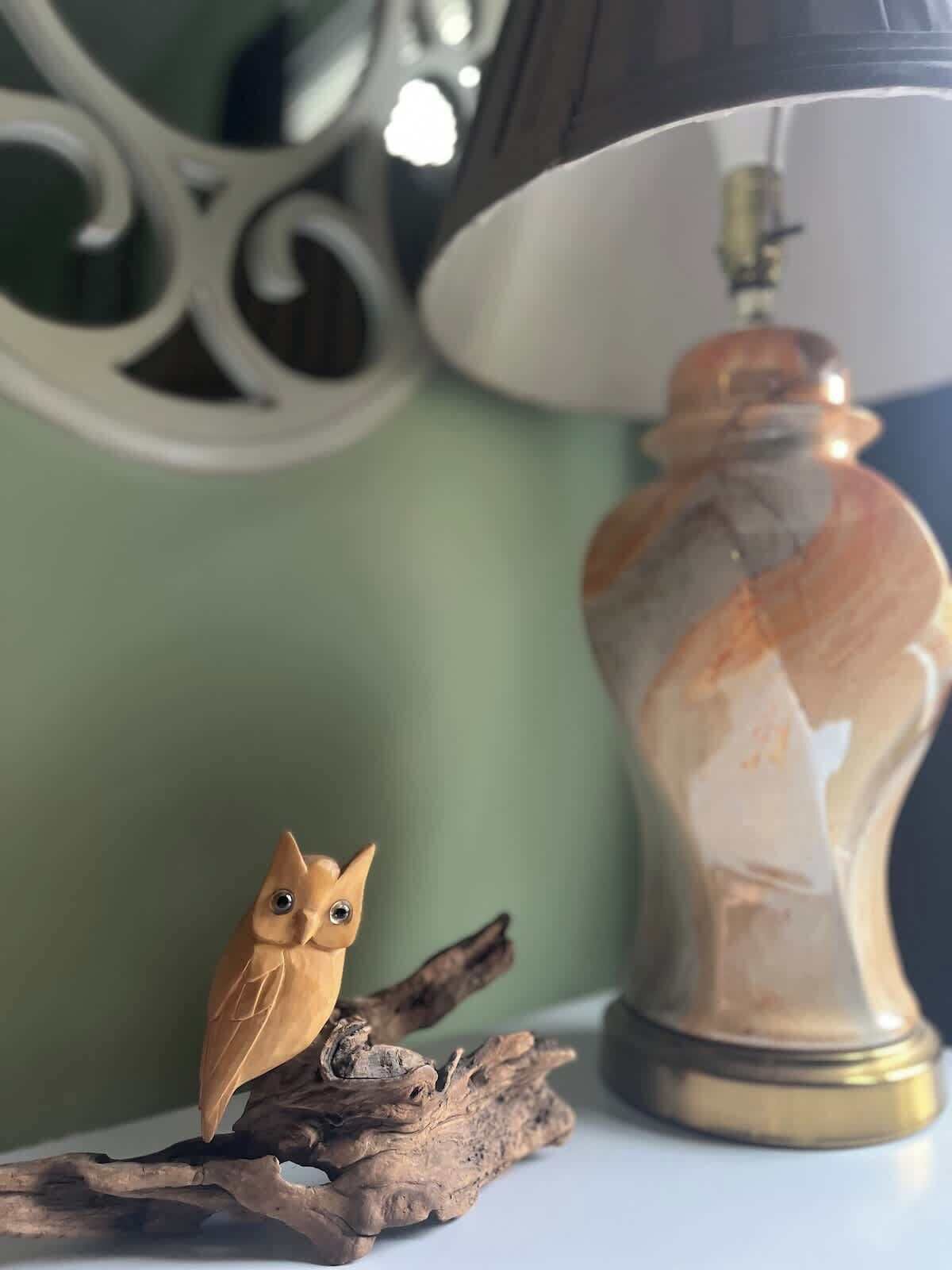 A lamp with a reflective surface and a small owl figurine on a branch.