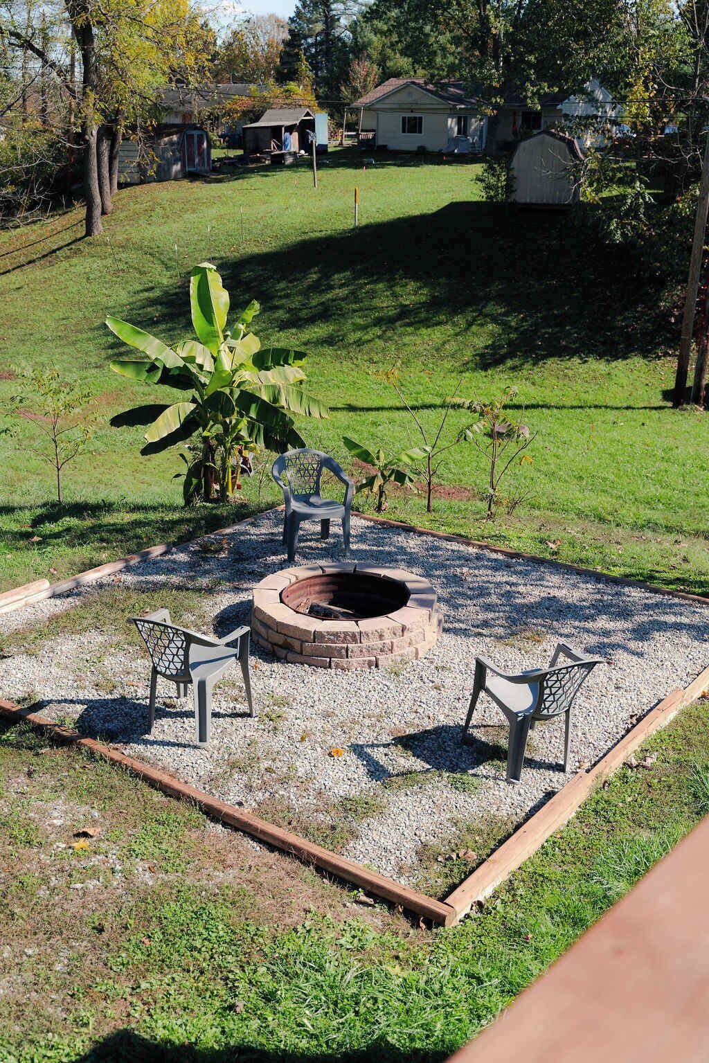 A backyard with a fire pit, two chairs, and a small garden area.