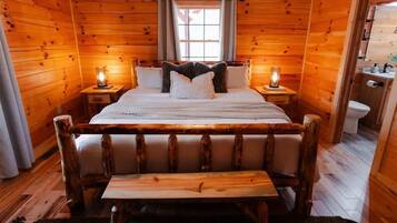 Un dormitorio de cabaña de madera con una cama, mesitas de noche, un banco y una ventana.