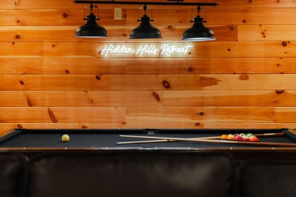Uma mesa de bilhar com um letreiro de neon que diz 'Hidden Hills Retreat'.