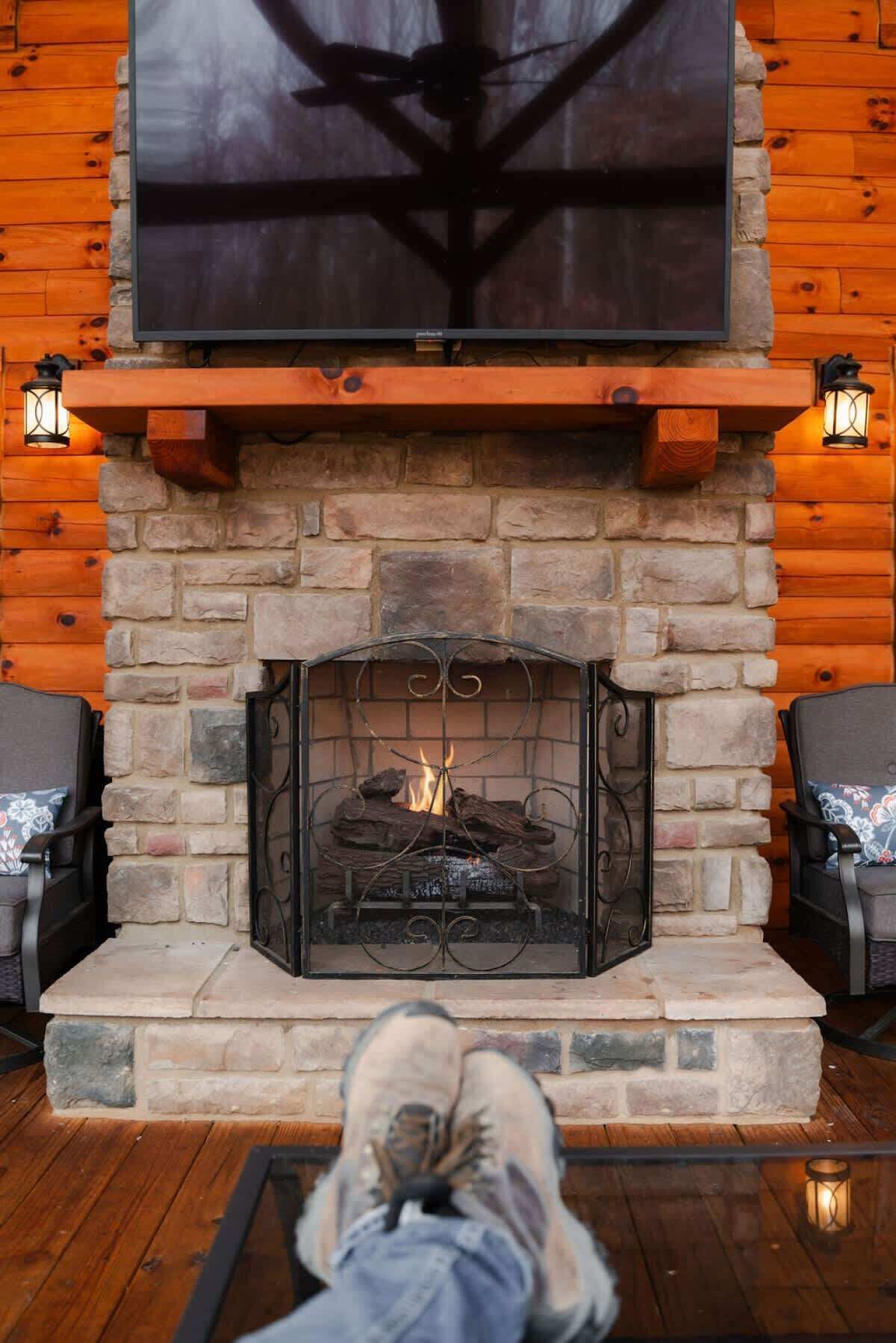 A stone fireplace with a fire, flanked by two chairs and two wall-mounted lanterns.
