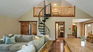 A spacious living area with a large wooden dining table, a built-in bench, a spiral staircase, and a cozy seating area with a sofa. - Tranquil Heights Cabin In Hocking Hills- HOT Tub! (Ray)