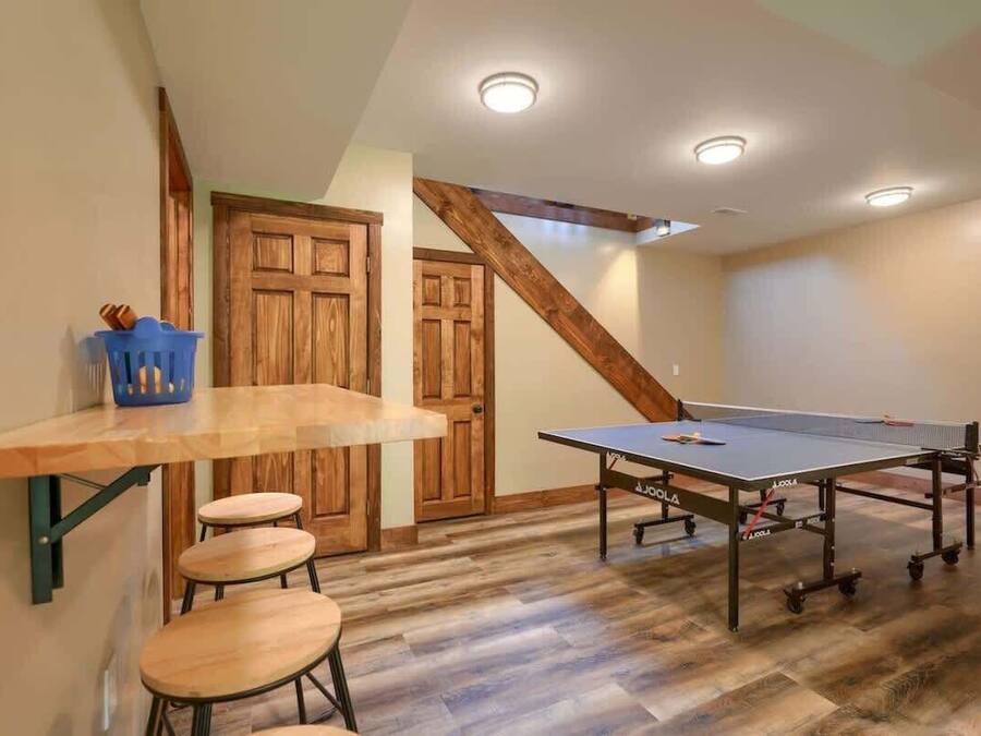 A room with a ping pong table, wooden flooring, and a high ceiling with recessed lighting.