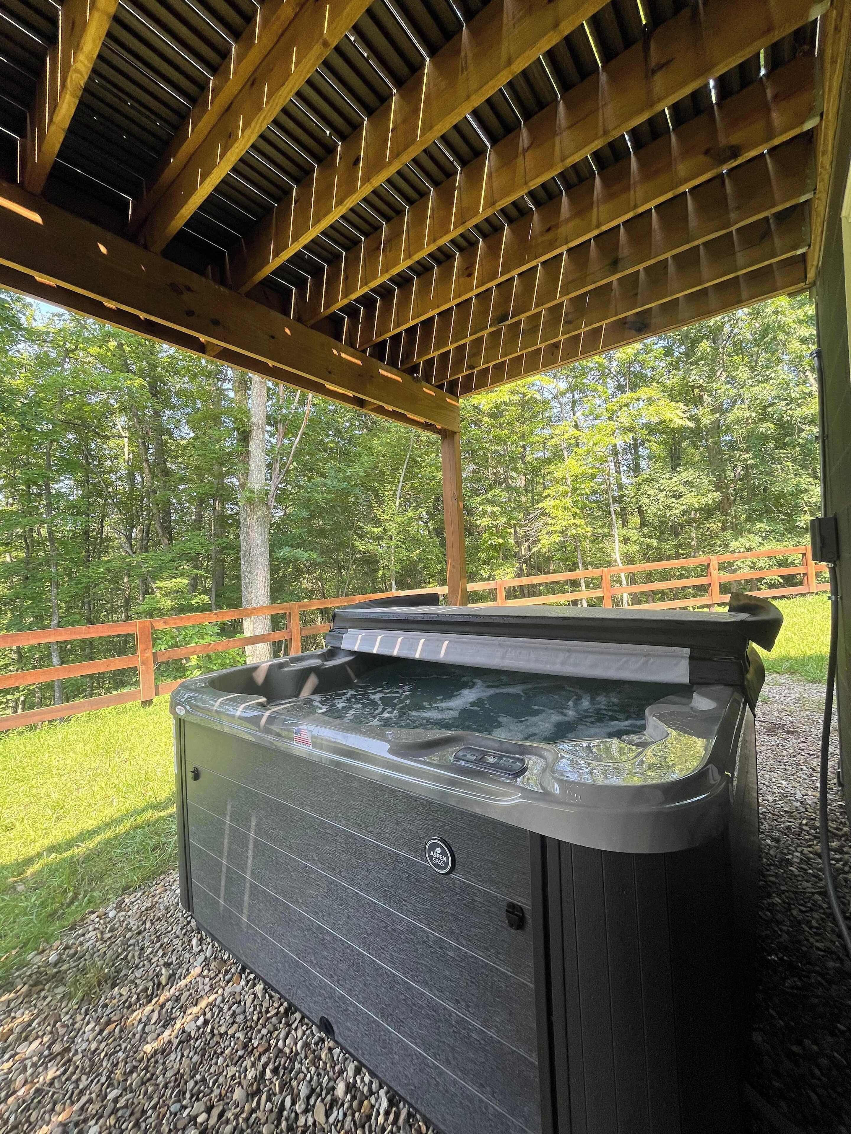 A hot tub under a wooden pergola with a wooden deck and a wooden fence in the background.