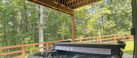 A hot tub under a wooden pergola with a wooden deck and a wooden fence in the background.
