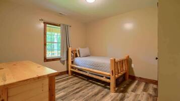 Una habitación pequeña con una cama individual, un marco de madera, un escritorio y una ventana con cortinas.