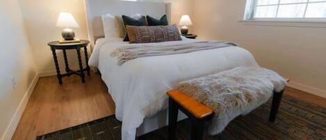 A neatly arranged bedroom with a large bed, two bedside tables, a bench, and a patterned rug.