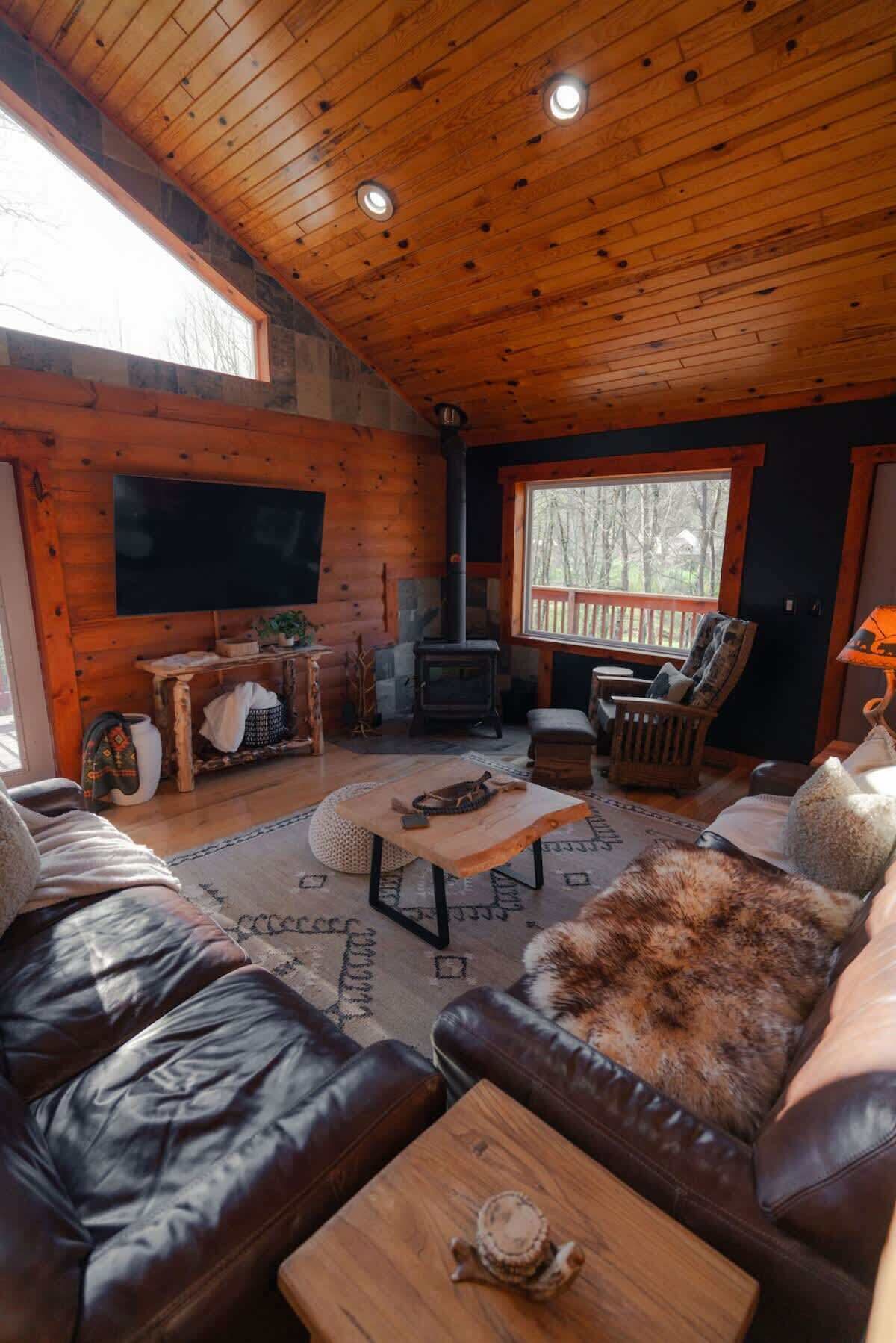 Un acogedor interior de cabaña con techo de madera, chimenea, sofás de cuero y televisor de pantalla plana.