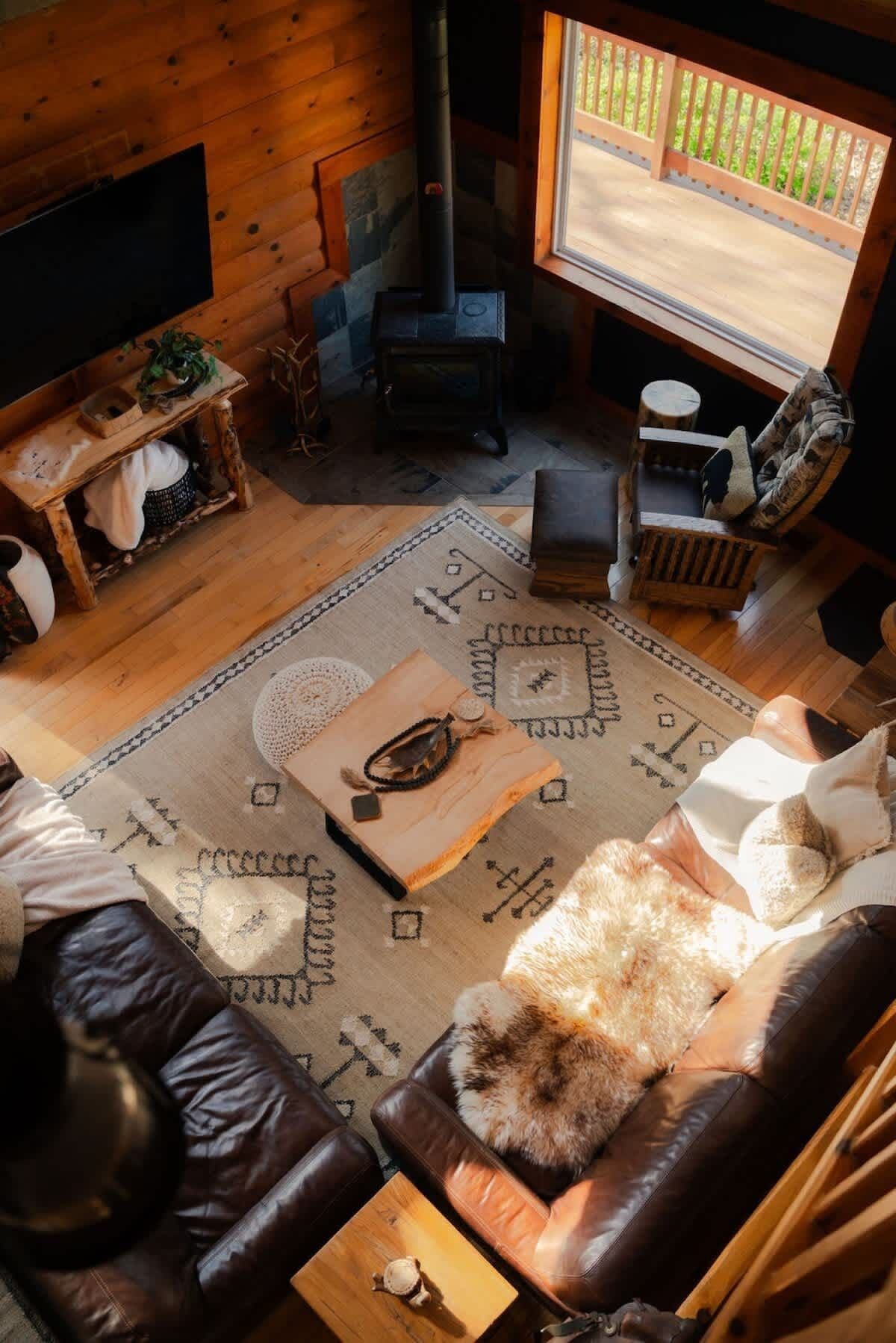 L’intérieur d’un chalet accueillant, avec un plancher en bois, une cheminée en pierre, un téléviseur, un canapé confortable et une vue par la fenêtre.