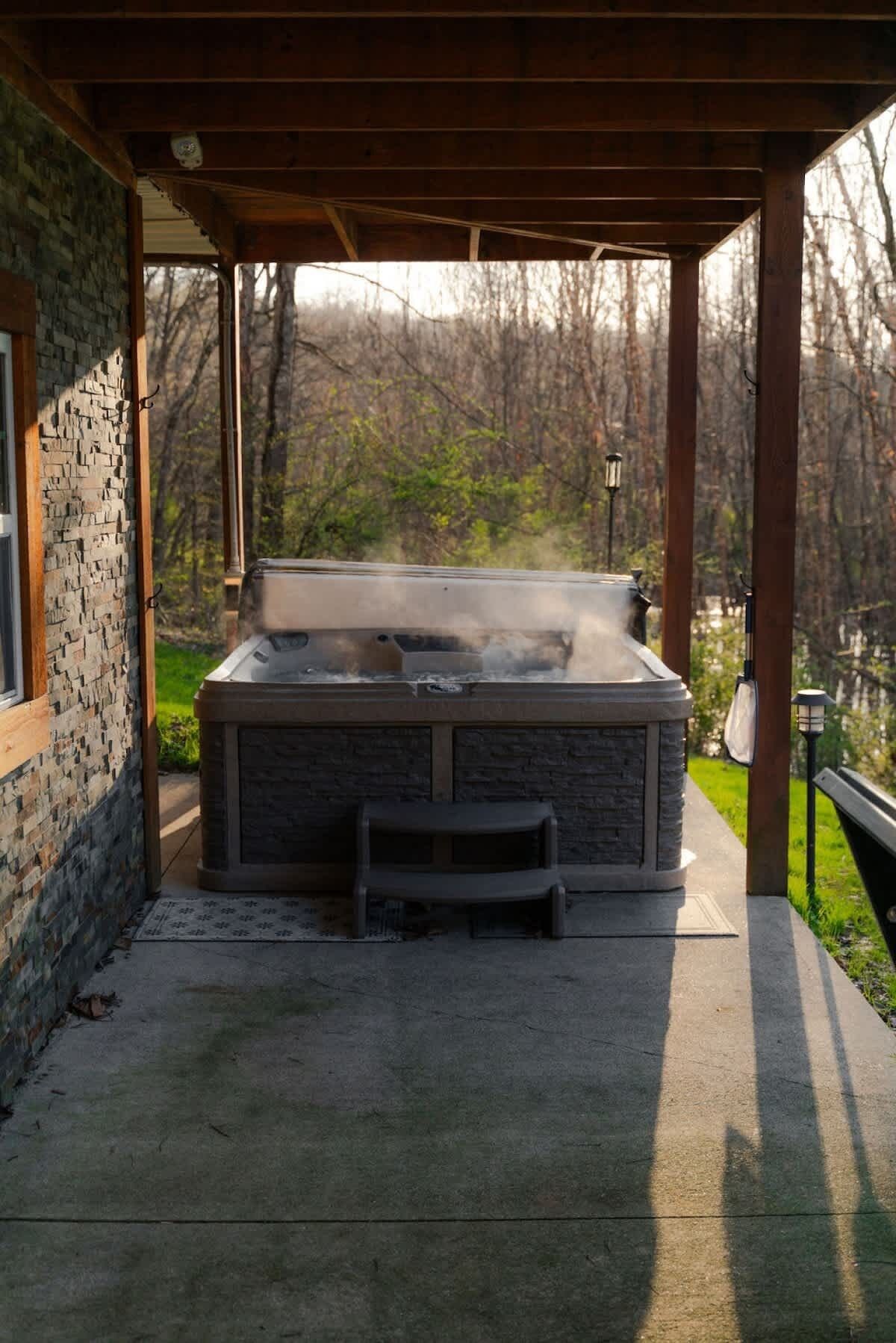 A hot tub under a wooden pergola with a stone wall on one side.