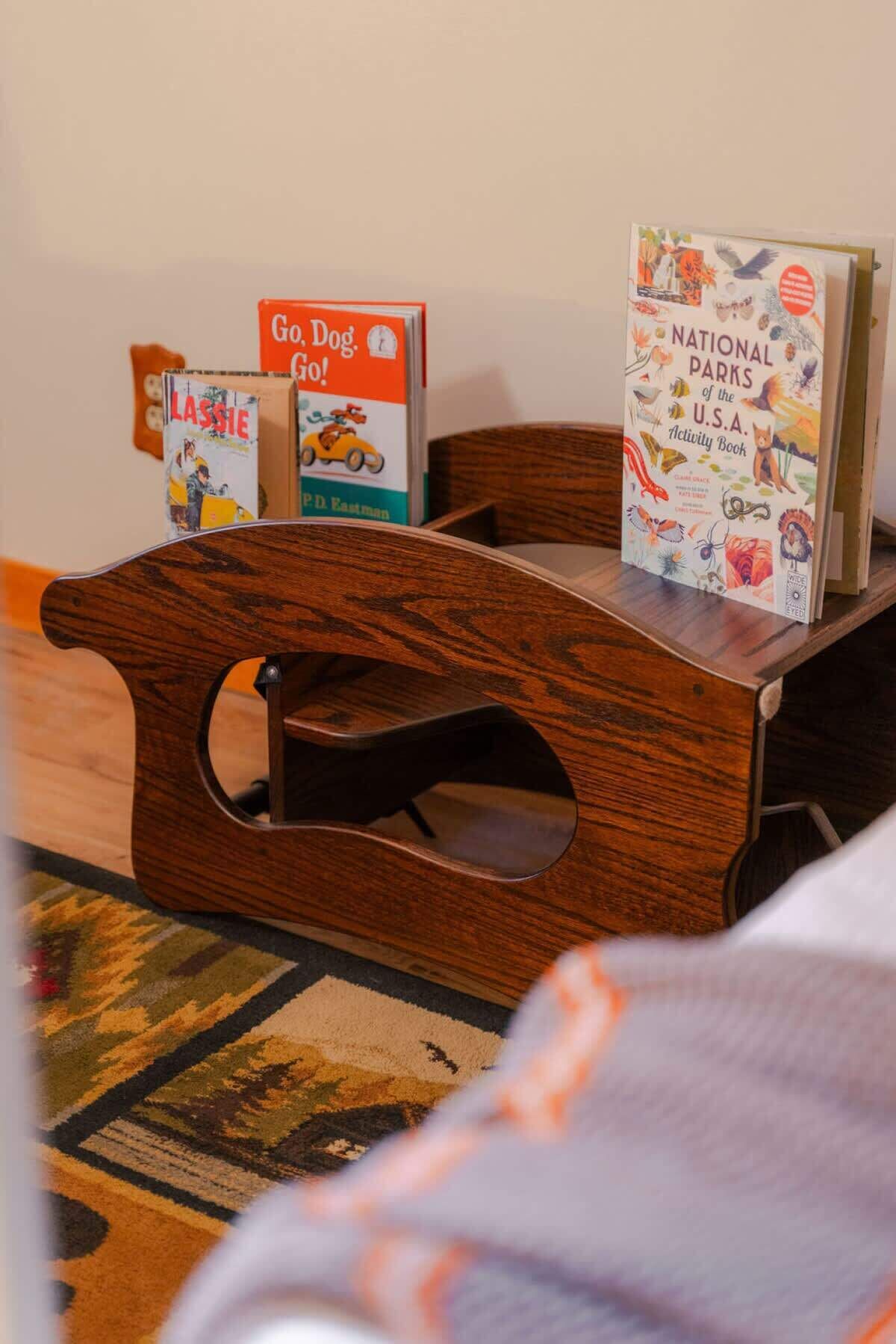 Un banco de madera con respaldo abierto, una pequeña mesa con libros y una alfombra estampada en el suelo.