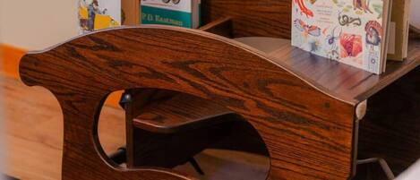 A wooden bench with a cut-out backrest, a small table with books, and a patterned rug on the floor.