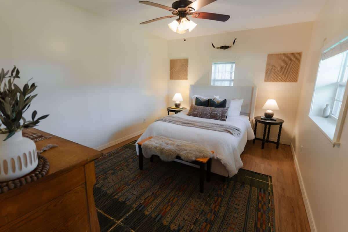 A bedroom with a bed, bedside tables, a ceiling fan, a window, and a decorative plant.