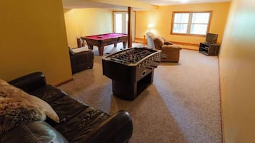 Una sala de estar con mesa de fútbol de mesa, mesa de billar, sofá y televisor.