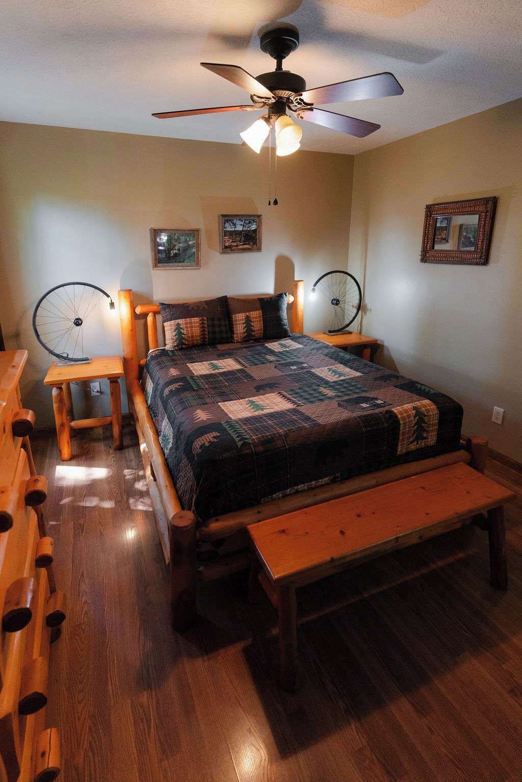 A cozy bedroom with a wooden bed, a bench, a ceiling fan, and two wall-mounted bicycle wheels.