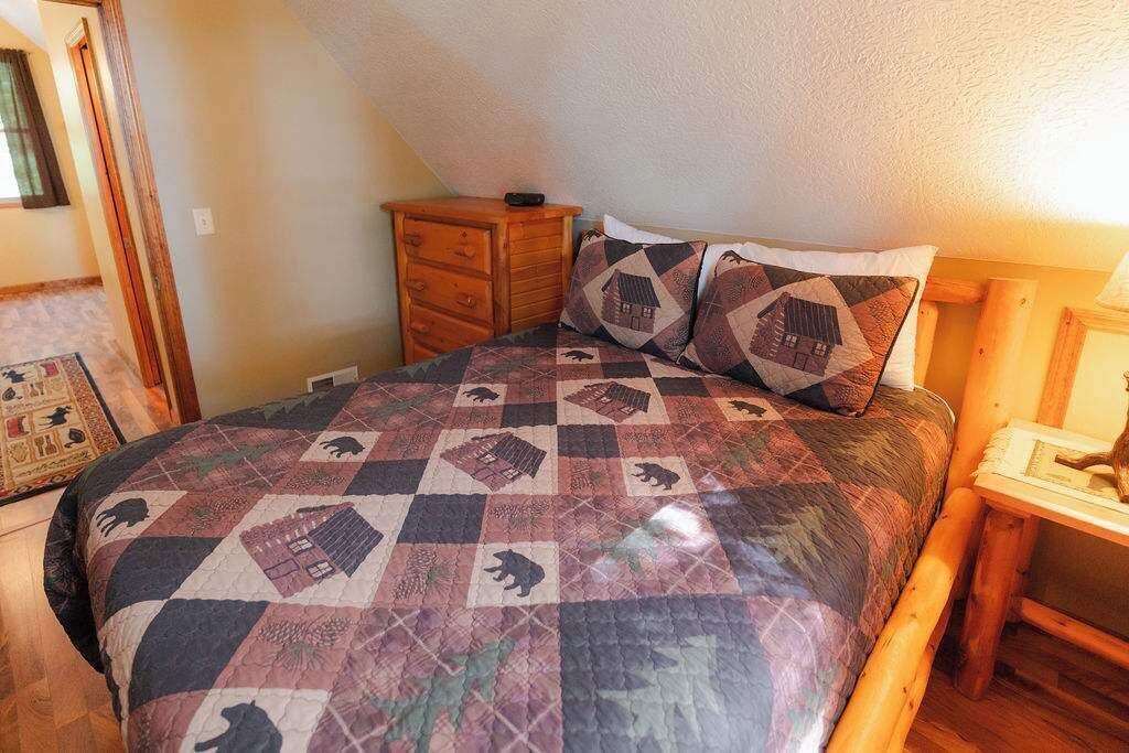 A bedroom with a quilted bedspread featuring animal patterns, a wooden nightstand, and a small wooden dresser.
