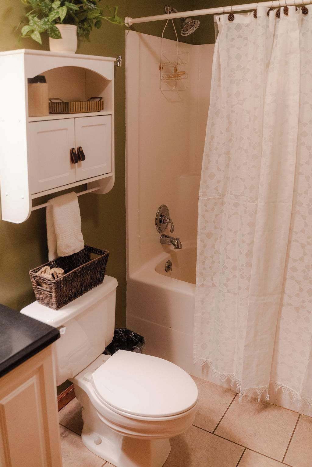 A bathroom with a white toilet, a bathtub, a shower curtain, and a small shelf with a basket and slippers.