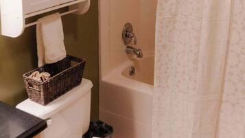 A bathroom with a white toilet, a bathtub, a shower curtain, and a small shelf with a basket and slippers.