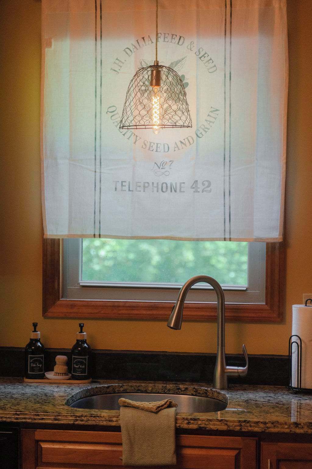A kitchen with a window, a sink, and a faucet. There is a bottle of soap and a towel on the counter.