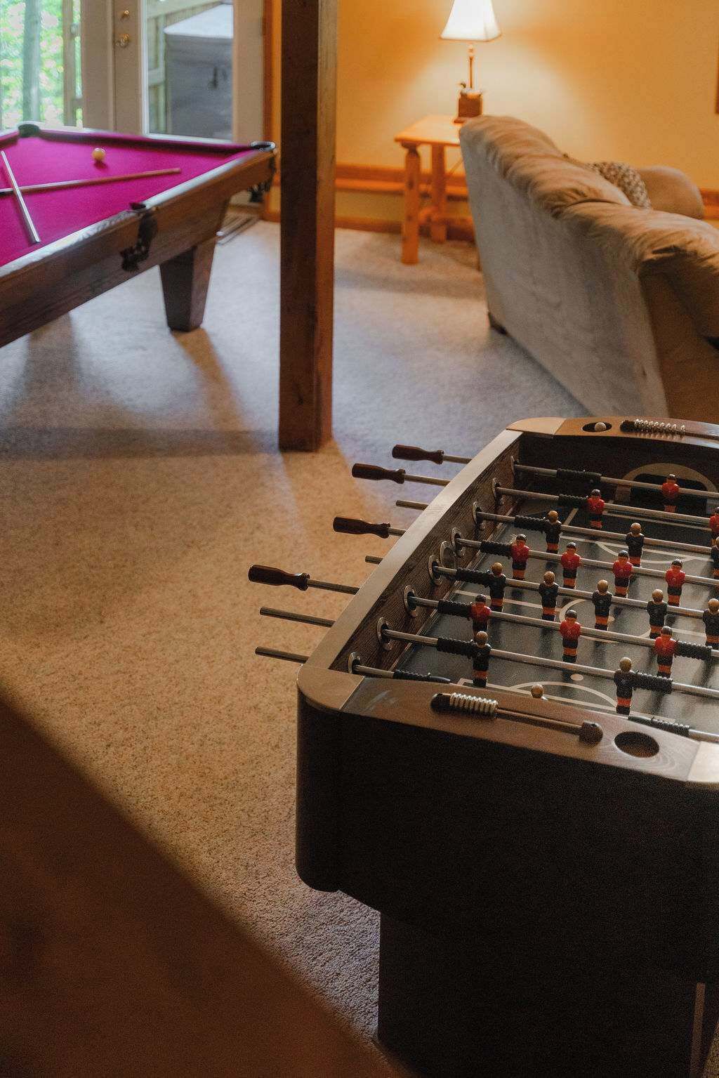 Una mesa de fútbol de mesa y una mesa de billar en una habitación con un sofá y una lámpara.