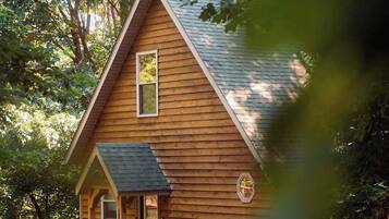 Une cabane en bois avec un toit à forte pente, un porche à l’avant et un petit escalier menant à l’entrée.