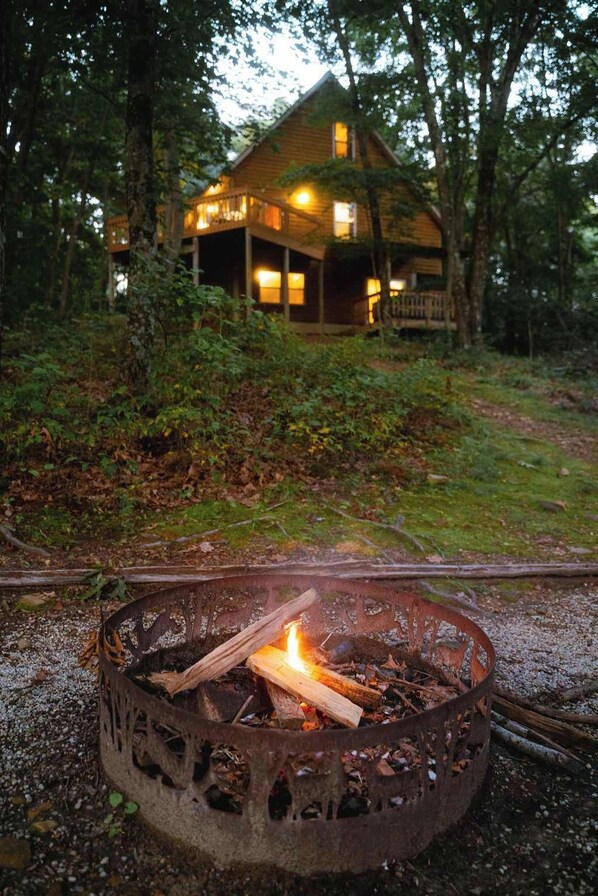 A rustic cabin with a fire pit in the foreground, surrounded by dense forest. - Cheerful Two Bdrm Cabin With Hot Tub & Pet Friendly (Rockbridge)