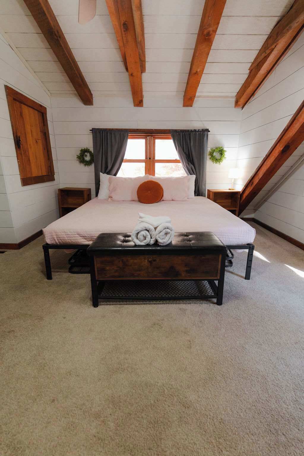 A bedroom with a large bed, a bench, and a window with curtains.