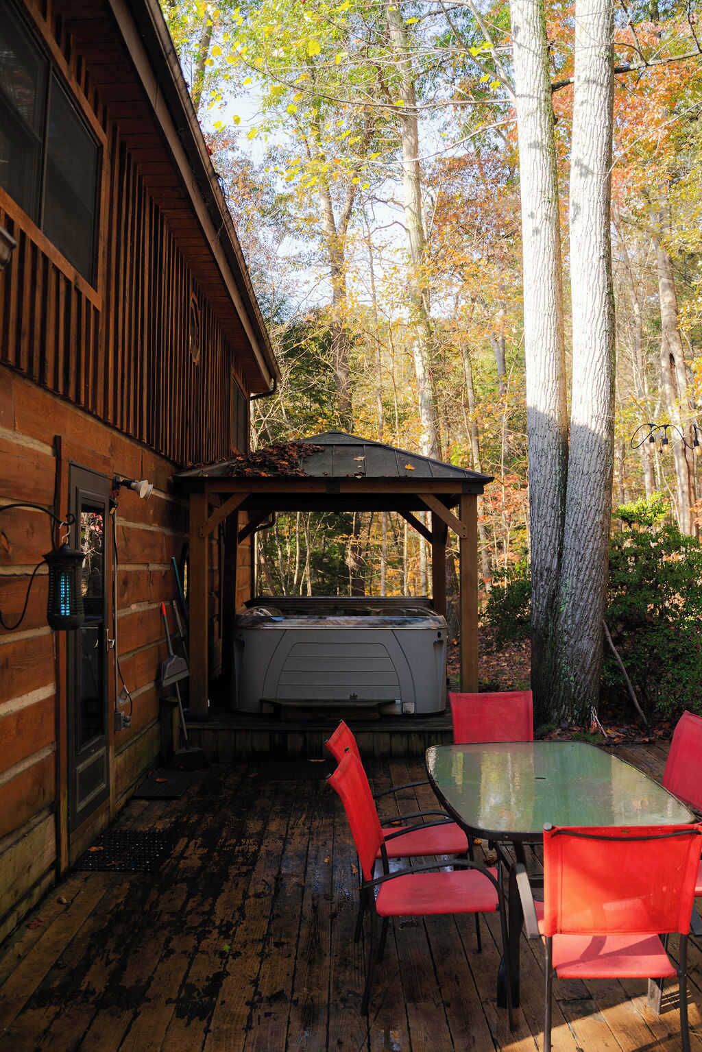 Una cabaña de madera con un patio que cuenta con mesa y sillas, un jacuzzi y una zona de estar cubierta.