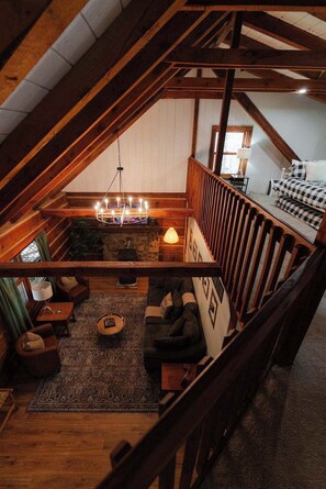 A cozy loft bedroom with a sloped ceiling, a stone fireplace, a chandelier, and a bed with checkered bedding. - Outdoors Sleeps7 Family Getaway Fun Arcade (Rockbridge)
