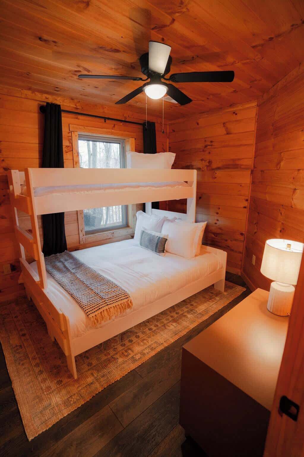 Habitación con literas, ventilador de techo, una ventana y una mesita de noche con lámpara.