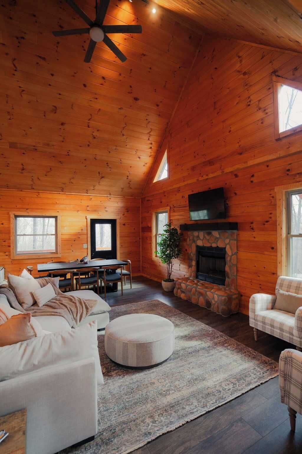 A log cabin interior with a fireplace, a dining area, and a seating area with a sofa and ottoman.
