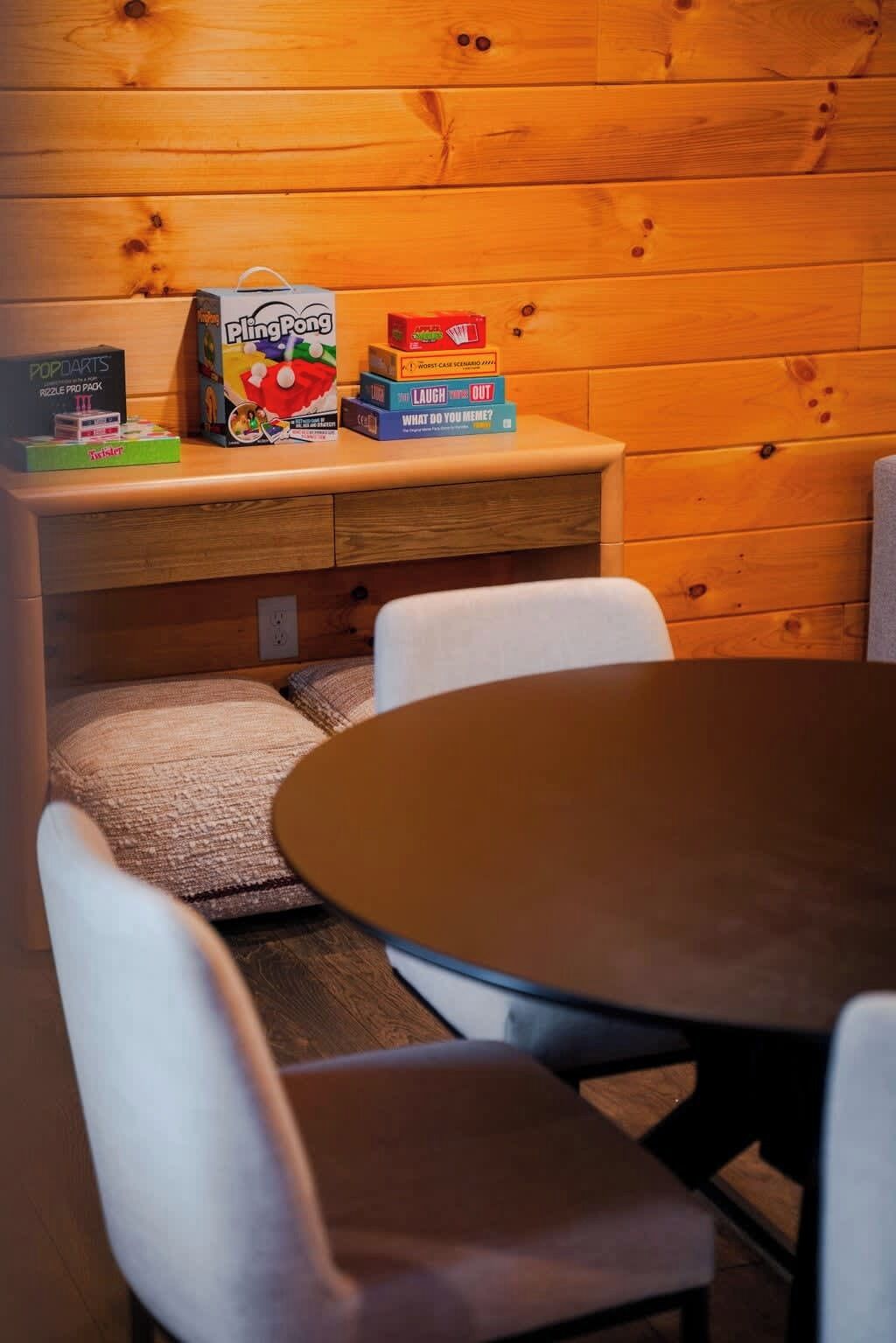 Un interior de madera con una mesa y sillas, una estantería con juegos de rompecabezas y una caja de Pling Pong.
