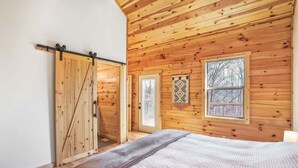 Un dormitorio con paneles de madera, una cama, un acceso corredizo y dos ventanas.