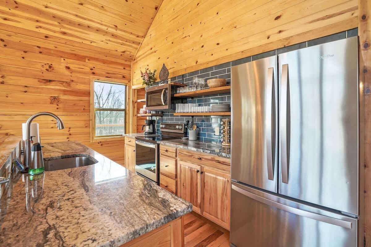A modern kitchen with wooden walls, granite countertops, stainless steel appliances, and a window overlooking a snowy landscape.
