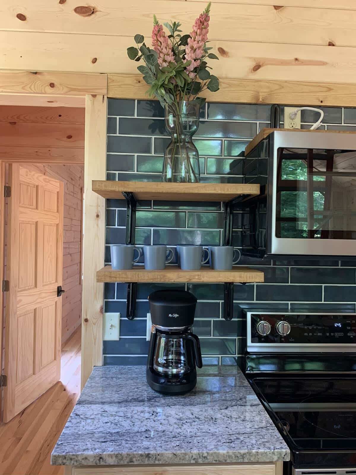 A kitchen with a coffee maker, a stove, and a shelf with mugs.