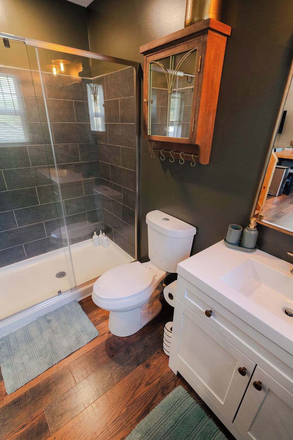 A modern bathroom with a glass-enclosed shower, a white toilet, and a wooden cabinet with a mirror.