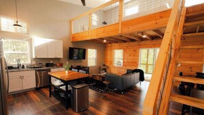 A spacious loft-style room with a kitchen, dining area, and seating area, featuring wooden floors and a lofted sleeping area. - The Treetop Retreat Family Getaway in Scenic Hocking Hills (Logan)