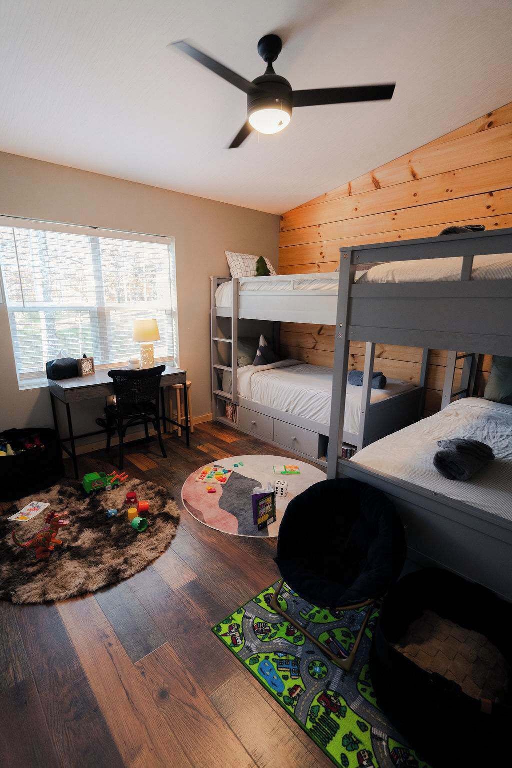 A room with bunk beds, a desk, a chair, and a ceiling fan.