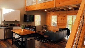 A spacious loft-style living area with a kitchen, wooden floors, and a mezzanine level. - The Treetop Retreat Family Getaway in Scenic Hocking Hills (Logan)