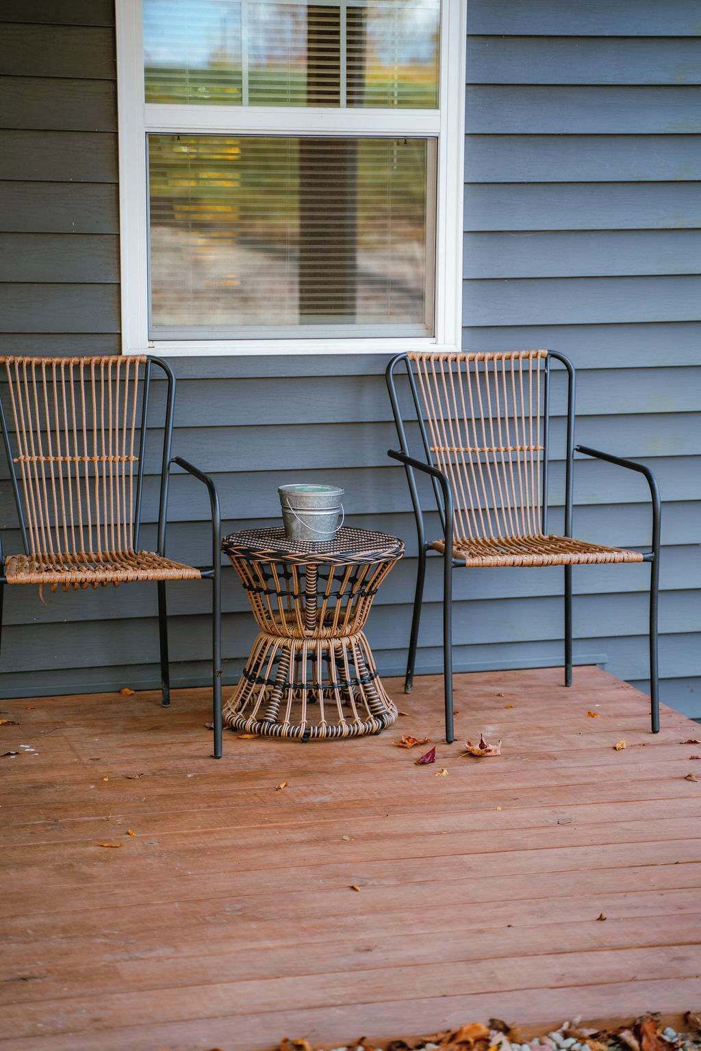 A wooden deck with two wicker chairs and a small table.