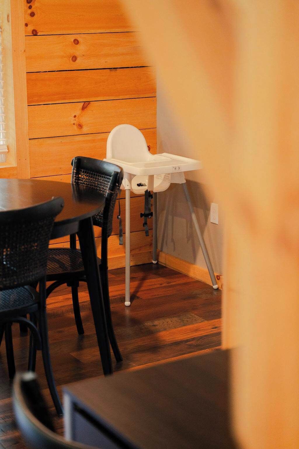 A wooden interior with a dining table and chairs, a white high chair, and a wall-mounted heater.