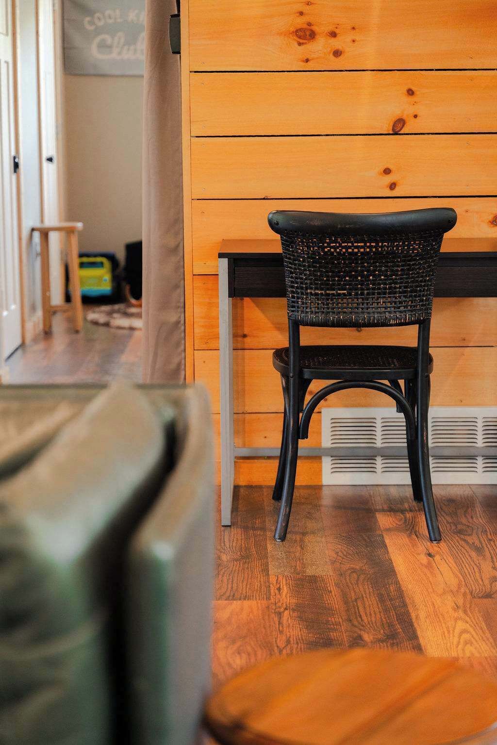 A room with a wooden wall, a black woven chair, and a wooden floor.