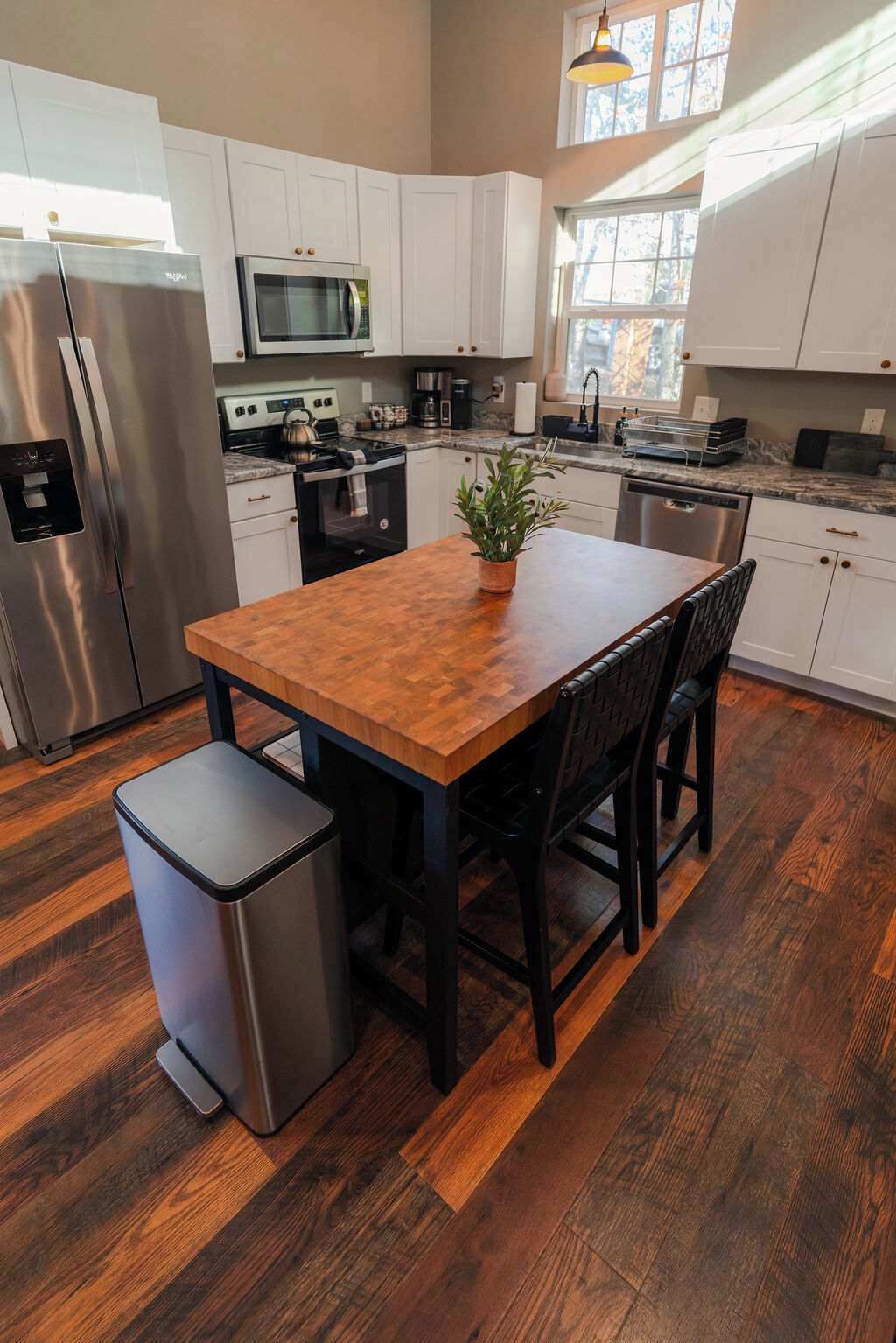 A kitchen with white cabinets, stainless steel appliances, a wooden dining table, and a trash bin.